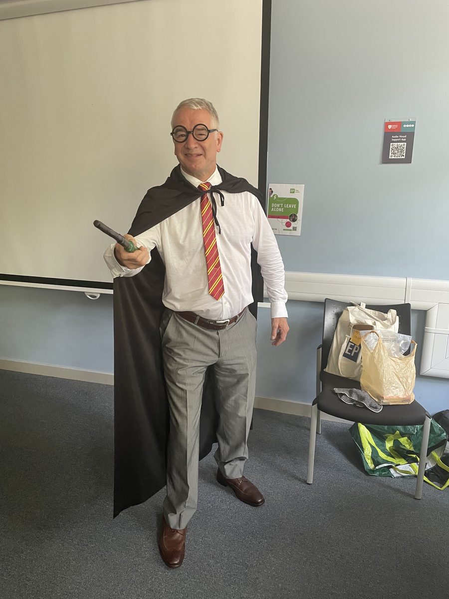 Eddie Barber in the classroom in Harry Potter costume, with cape, round glasses and wand